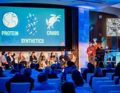 Sessió plenària del BlueInvest Day 2026 a Brussel·les amb una pantalla que il·lustra biotecnologia blava i un panell d'experts assegut a l'escenari.