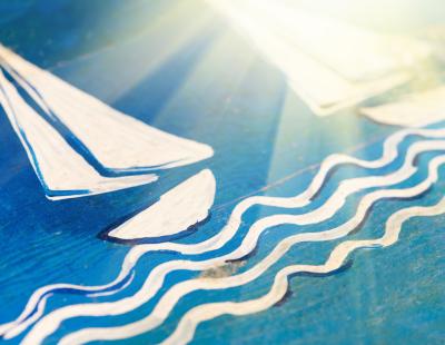 Velero de vela blanca y olas pintados a mano sobre una tabla de madera azul iluminada por el sol.