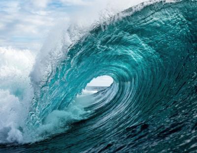 Onada de color turquesa que es trenca i forma un tub sobre el mar obert, sota un cel ennuvolat