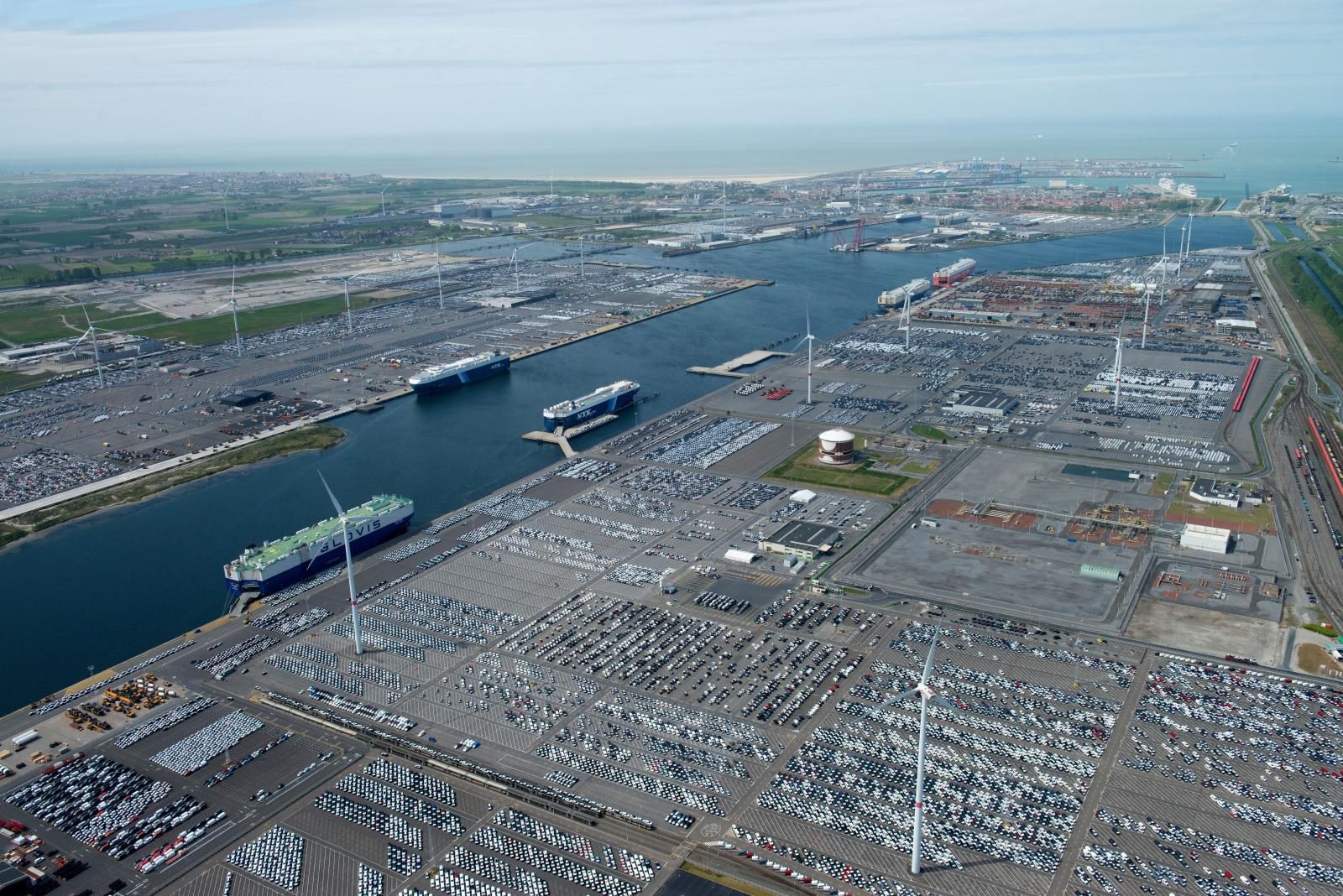 Vista aérea de la dársena interior de Zeebrugge con miles de coches en stock, car carriers atracados y aerogeneradores en el puerto de Amberes-Brujas.
