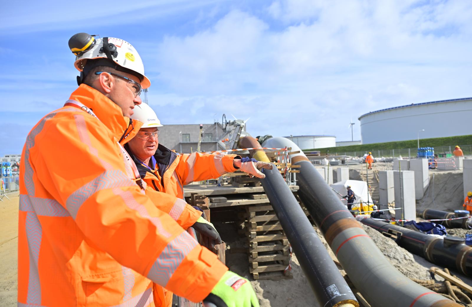 Dos trabajadores con equipos de protección revisan las tuberías en la construcción de la estación de compresión del proyecto Porthos de transporte y almacenamiento de CO₂ en el puerto de Róterdam