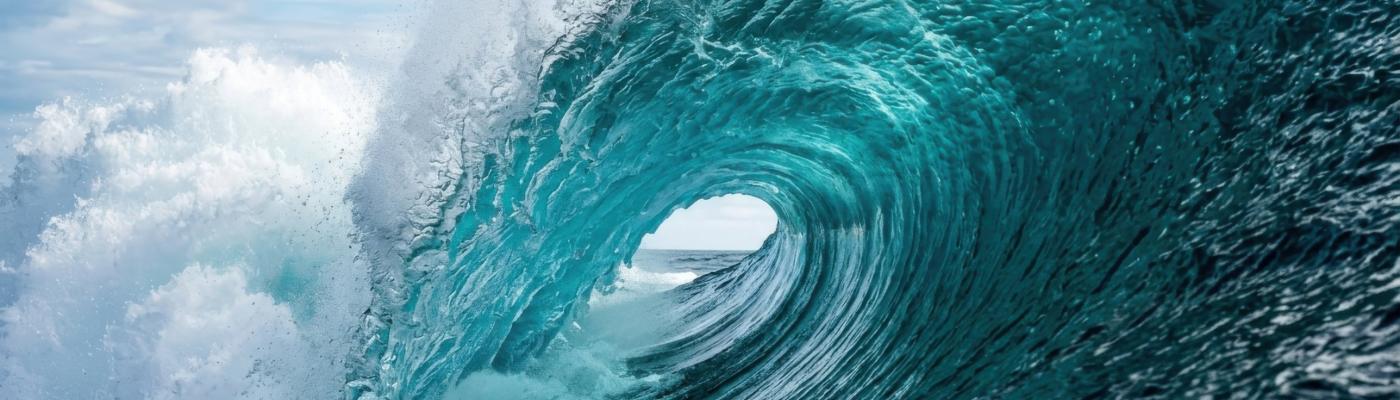 Onada de color turquesa que es trenca i forma un tub sobre el mar obert, sota un cel ennuvolat