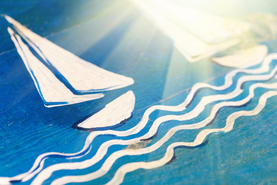 Velero de vela blanca y olas pintados a mano sobre una tabla de madera azul iluminada por el sol.