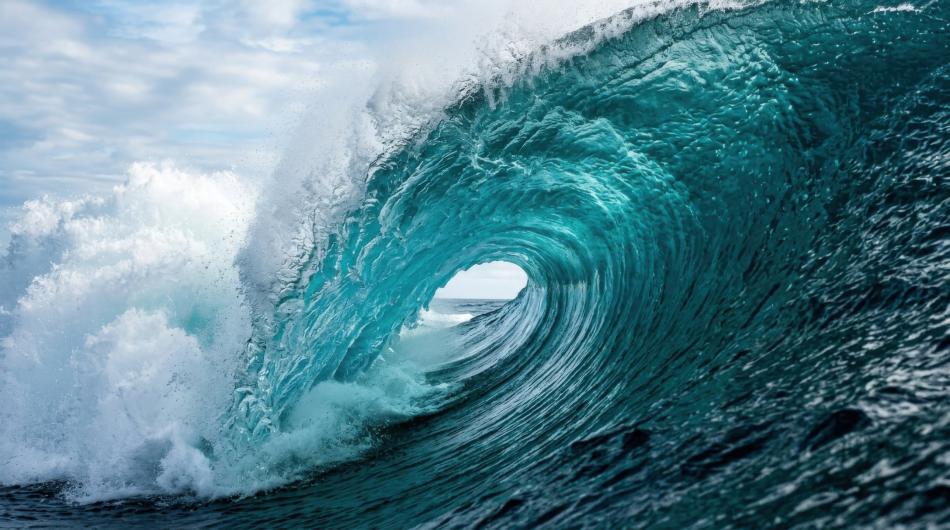 Onada de color turquesa que es trenca i forma un tub sobre el mar obert, sota un cel ennuvolat