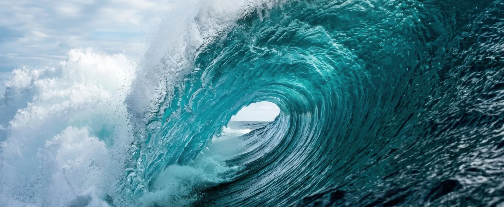 Onada de color turquesa que es trenca i forma un tub sobre el mar obert, sota un cel ennuvolat