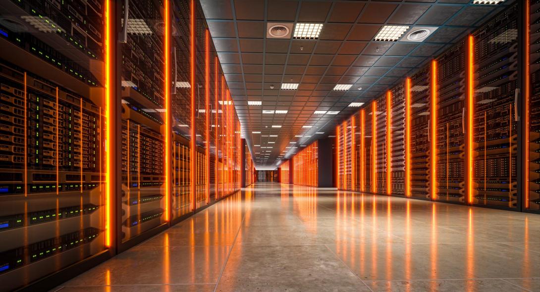 Interior de un centro de datos moderno con largos pasillos flanqueados por racks de servidores iluminados con luz naranja y verde, mostrando la infraestructura tecnológica necesaria para el procesamiento y almacenamiento de datos.