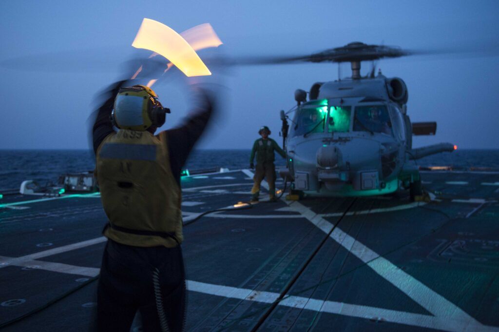 Un mariner assignat al destructor de míssils guiats USS Farragut (DDG 99) fa senyals a un helicòpter MH-60R Sea Hawk. (Foto de la Marina dels EUA, Especialista en Comunicació de Masses de 3a Classe Jackie Hart/Released)